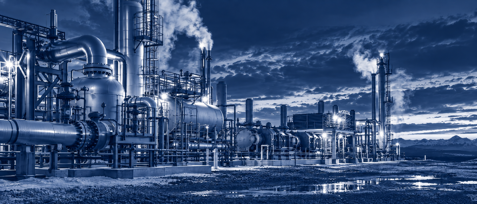 A gas processing plant lit at night with mountains behind it